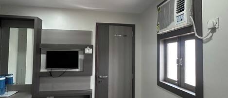 Ein Hotelzimmer mit Fernseher, Klimaanlage und einer Tür zu einem weiteren Raum.