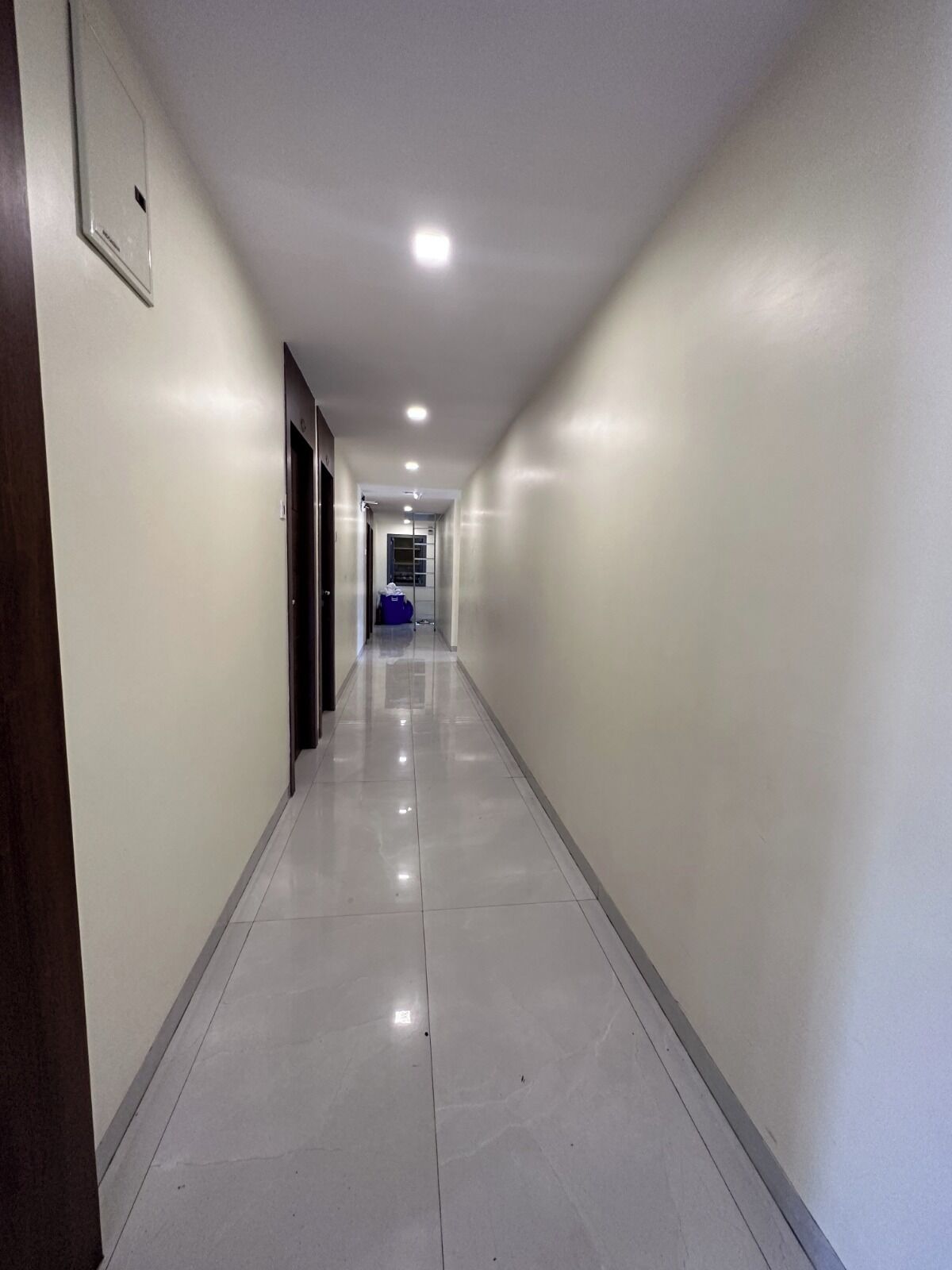 A long, narrow hallway with white walls and a shiny tiled floor.
