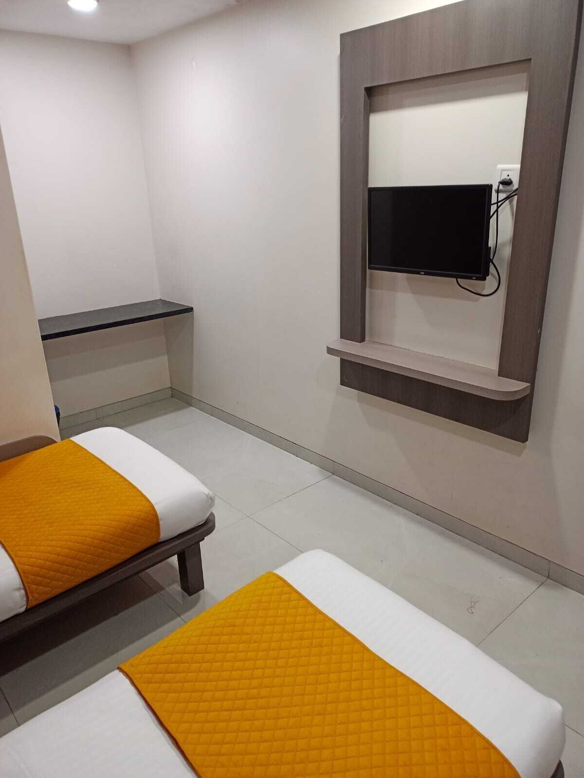 A hotel room with two beds, a TV mounted on the wall, and a small shelf.