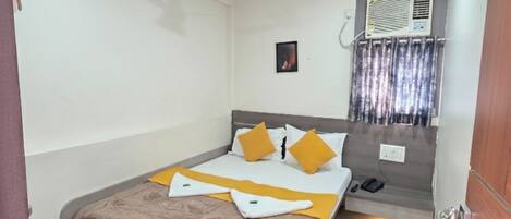 Quarto de hotel com cama, mesa de cabeceira, ar-condicionado fixado na parede e janela com cortinas.