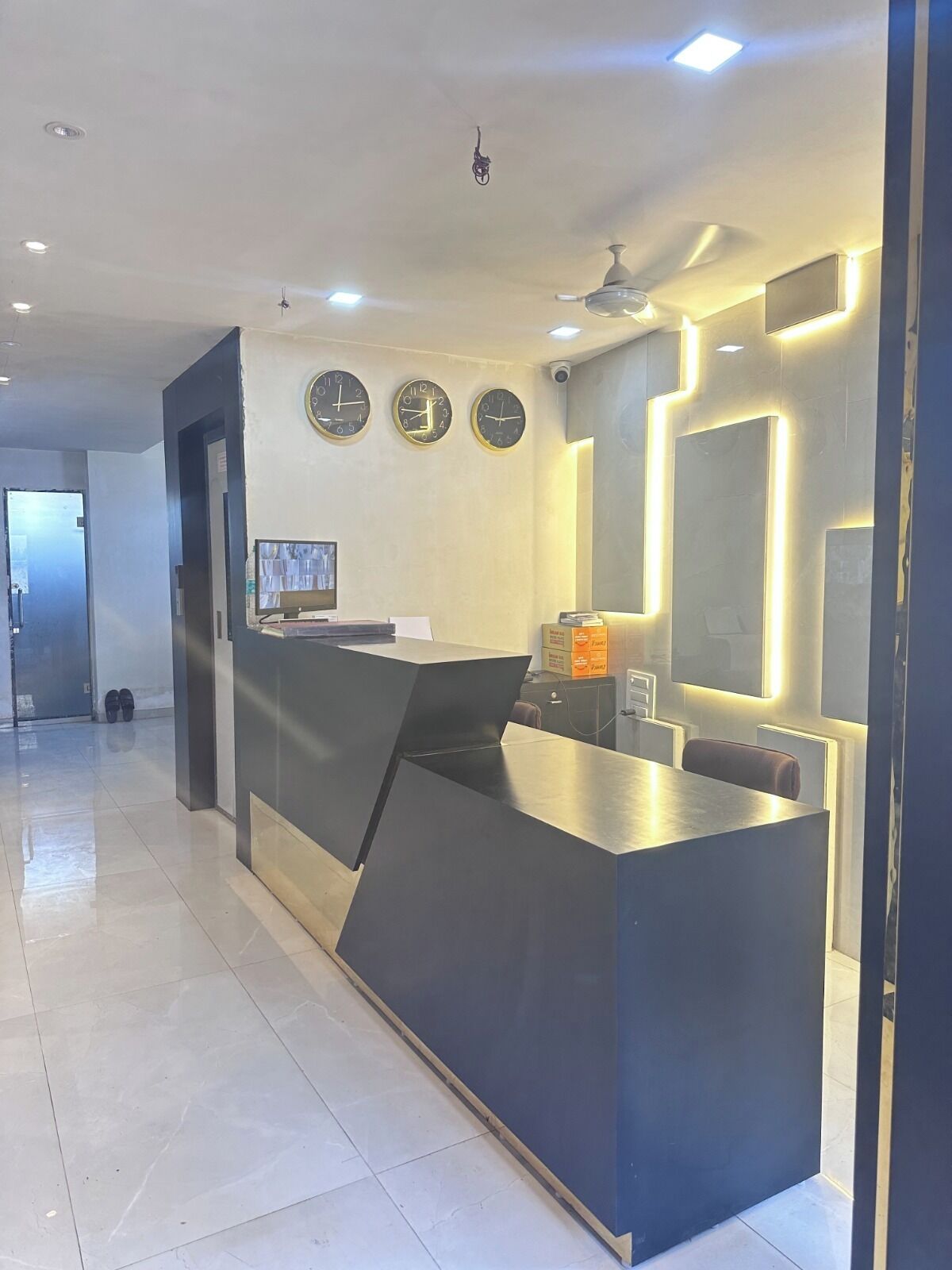 A modern reception desk with a digital screen, three wall clocks, and a ceiling fan.