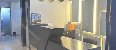A modern reception desk with a digital screen, three wall clocks, and a ceiling fan.