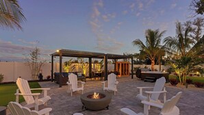 Un patio al aire libre con sillas Adirondack, un pozo de fuego, una pérgola y una zona de parrillada.