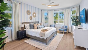 Un dormitorio con cama, mesita de noche, sillón y televisor sobre un aparador.