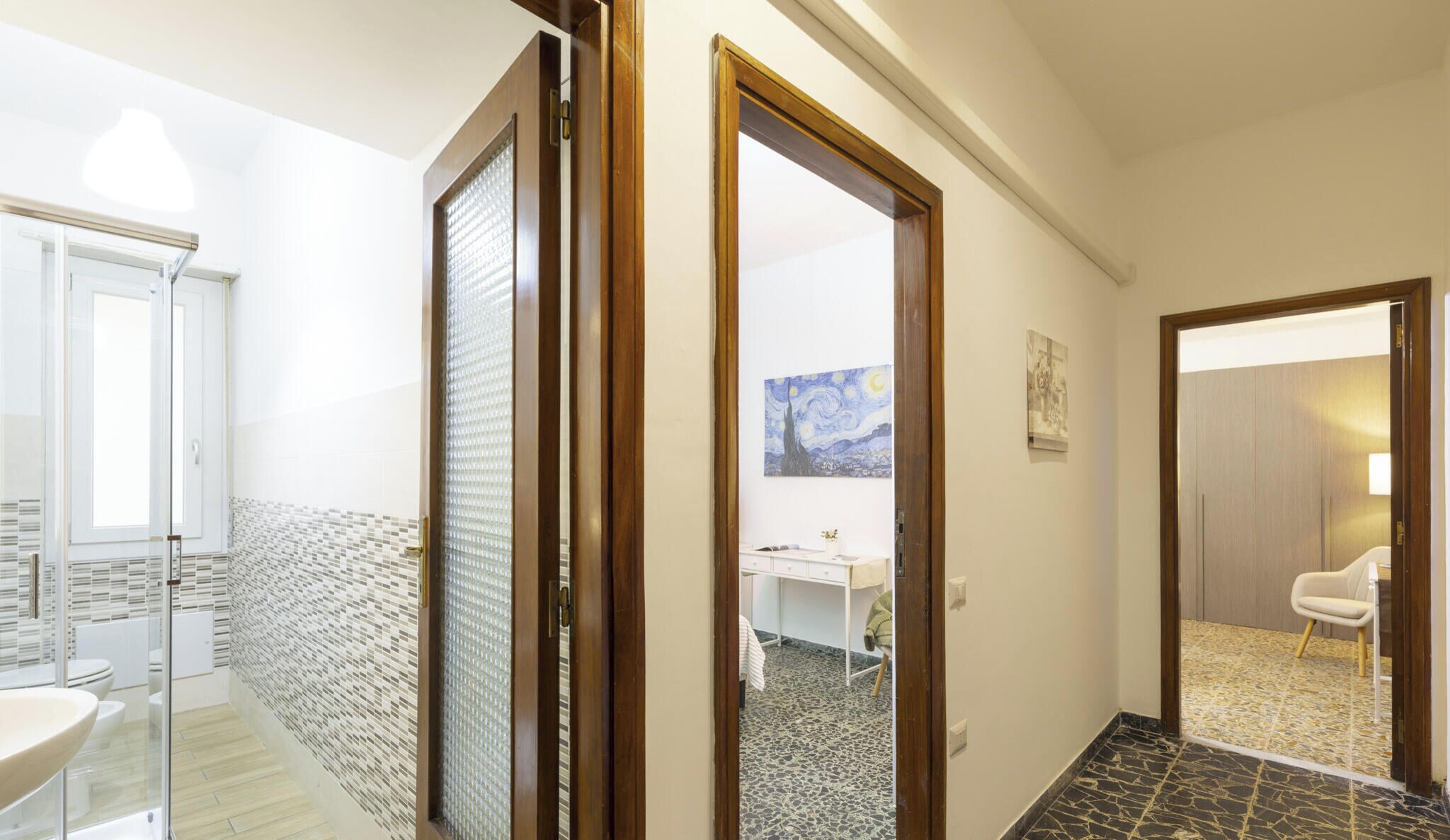Un couloir d’hôtel avec une salle de bain à gauche, un espace repas au centre et une chambre avec une chaise à droite.