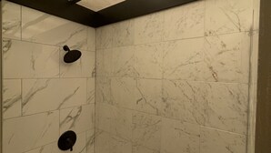 Een badkamer met een badkuip, een douchekop en een toiletrolhouder aan de muur.
