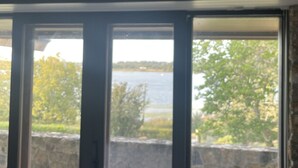 Een kamer met een grote schuifglazen deur die leidt naar een balkon met uitzicht op een meer en bomen.