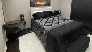 Een slaapkamer met een bed, een bureau, een stoel, een witte vloerkleed en een schilderij van een waterval aan de muur.