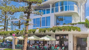 A modern building with multiple floors, large windows, and outdoor seating with umbrellas. - The Bay Apartments 15 - Rainbow Bay - Linen Provided - Min. 2 Night Stays Year Round (Coolangatta)