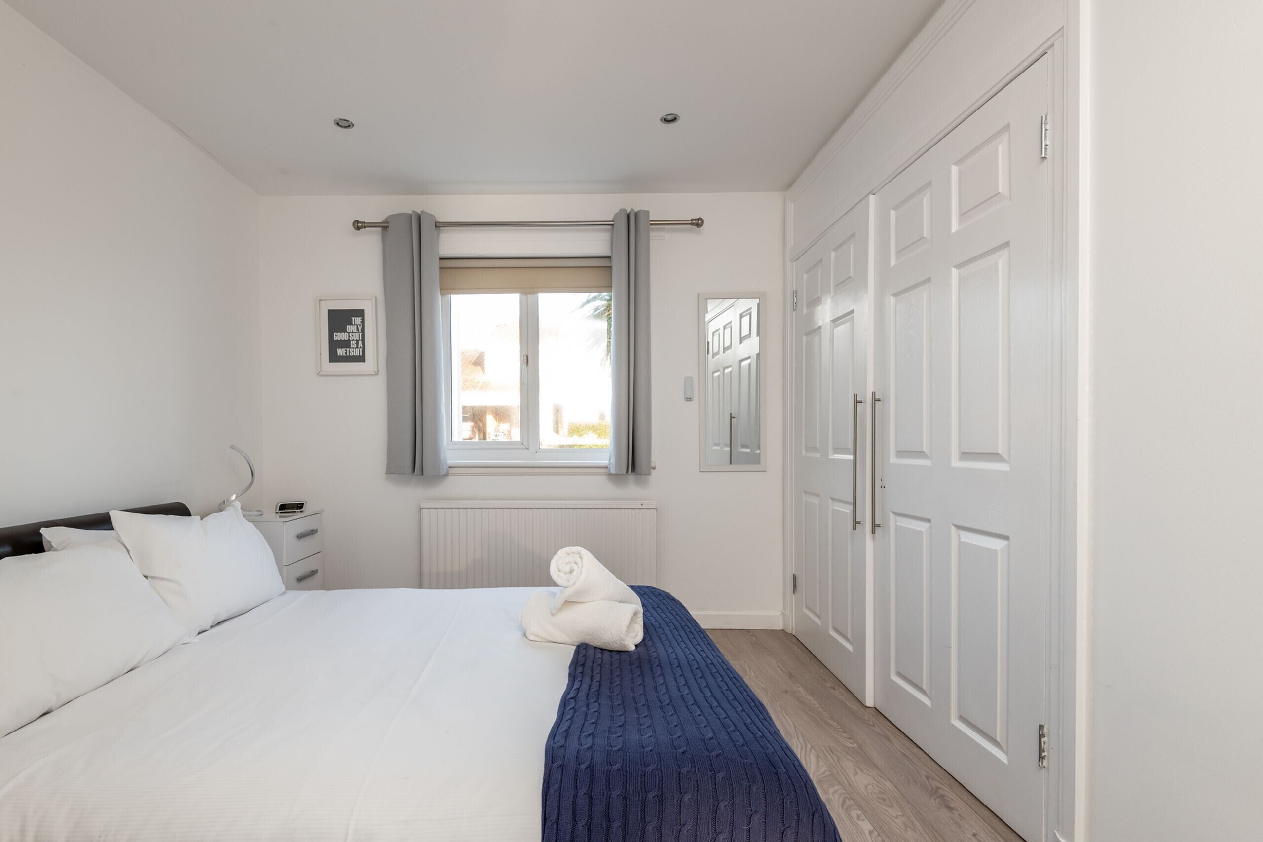 Een slaapkamer met een groot bed, een nachtkastje, een raam met gordijnen en een kledingkast.