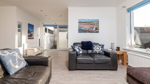 A modern living room with a leather sofa, a wooden coffee table, and a large window with a view of the sea. - Baird Place (No 26) | Elie (Elie)