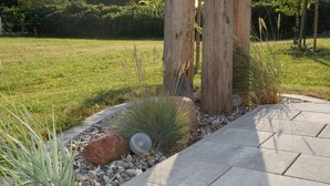 Ein angelegter Gartenbereich mit gepflastertem Weg, Holzpfosten und verschiedenen Pflanzen.