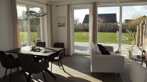 Ein geräumiger Raum mit Esstisch und Stühlen, einer Couch und großen Schiebeglastüren, die zu einem Außenbereich führen.