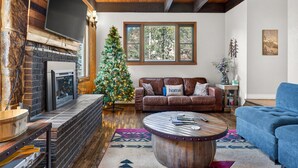 A cozy living room with a fireplace, a Christmas tree, a brown leather sofa, and a blue armchair.