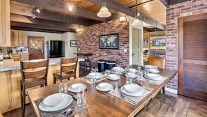 A spacious dining area with a long wooden table set for a meal, brick walls, and exposed wooden beams on the ceiling.