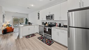 A modern kitchen with white cabinets, stainless steel appliances, and a large window overlooking a balcony. - Stylish BeltLine 1BR with Pool-View Balcony, EV Charging & Gym Next Door (Atlanta)