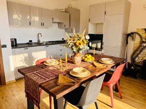 A modern kitchen with white cabinets, a dining table set with plates, glasses, and a vase of flowers. - Apartment Hamburg Balcony Lake View (Tignale)