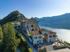 A historic building with a bell tower, a courtyard with outdoor seating, and a view of a lake and mountains. - Apartment Hamburg Balcony Lake View (Tignale)