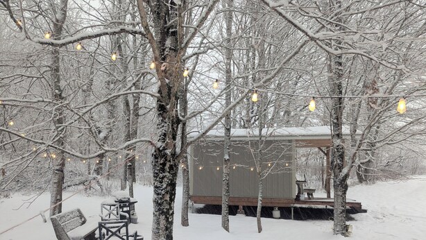 A snow-covered outdoor area with a wooden deck, a small shed, and string lights. - Romantic Tiny Cottage w/ Hot Tub & Fire Pit – Sunset Cottage #2 (Balmoral Mills)
