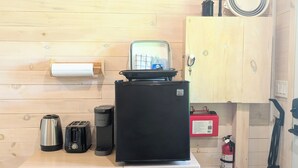 A compact kitchenette with a refrigerator, coffee maker, toaster, and a small cabinet. - Romantic Tiny Cottage w/ Hot Tub & Fire Pit – Sunset Cottage #2 (Balmoral Mills)