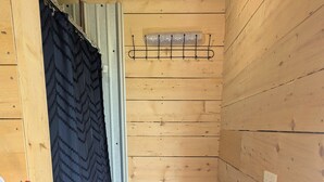 A small, wooden room with a white chair, a black curtain, and a hook on the wall. - Romantic Tiny Cottage w/ Hot Tub & Fire Pit – Sunset Cottage #2 (Balmoral Mills)