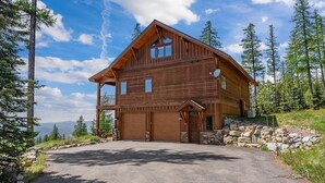 Une cabane en bois à deux étages, dotée d’un garage, entourée d’arbres et sous un ciel dégagé.