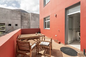A balcony with a wooden table and chairs, a small window, and a door leading to a kitchen area. - Apartamento 'Jimaguas' en Tamaduste, El Hierro, con terraza y vistas a la montaña (Tamaduste)
