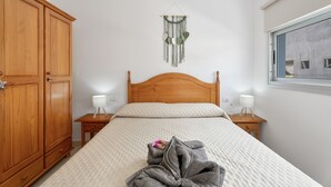 A bedroom with a wooden bed, two bedside tables with lamps, a wooden wardrobe, and a wall-mounted macrame decoration.