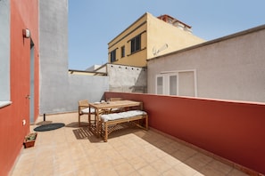 Un pequeño patio al aire libre con una mesa y banca de madera, una planta en maceta y una pared roja.