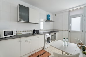 Una cocina moderna con armarios blancos, un microondas, una lavadora y un fregadero.