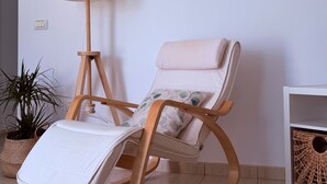 A room with a rocking chair, a floor lamp, a potted plant, and a woven basket on a shelf.