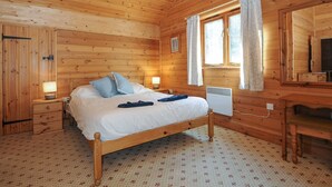 Een slaapkamer in een houten hutje met een bed, bedlampen, een bureau en een raam met gordijnen.