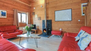 Een knus houten interieur met een open haard, leren banken in rood en een kaart aan de muur.