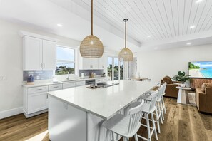 Una cucina moderna con mobili bianchi, una grande isola centrale e illuminazione a sospensione.
