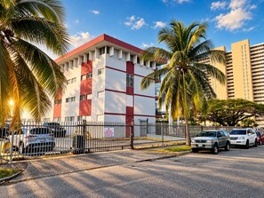 A building with a red and white facade, a gated entrance, and parked cars. - Serene Coastal Studio with King Bed & Balcony (Luquillo)