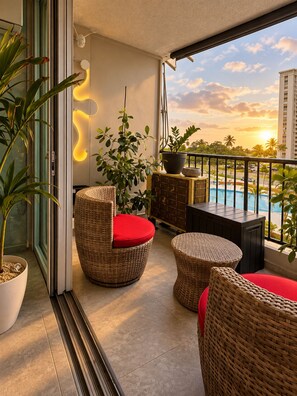 A balcony with wicker furniture, a potted plant, and a view of a swimming pool and buildings. - Serene Coastal Studio with King Bed & Balcony (Luquillo)