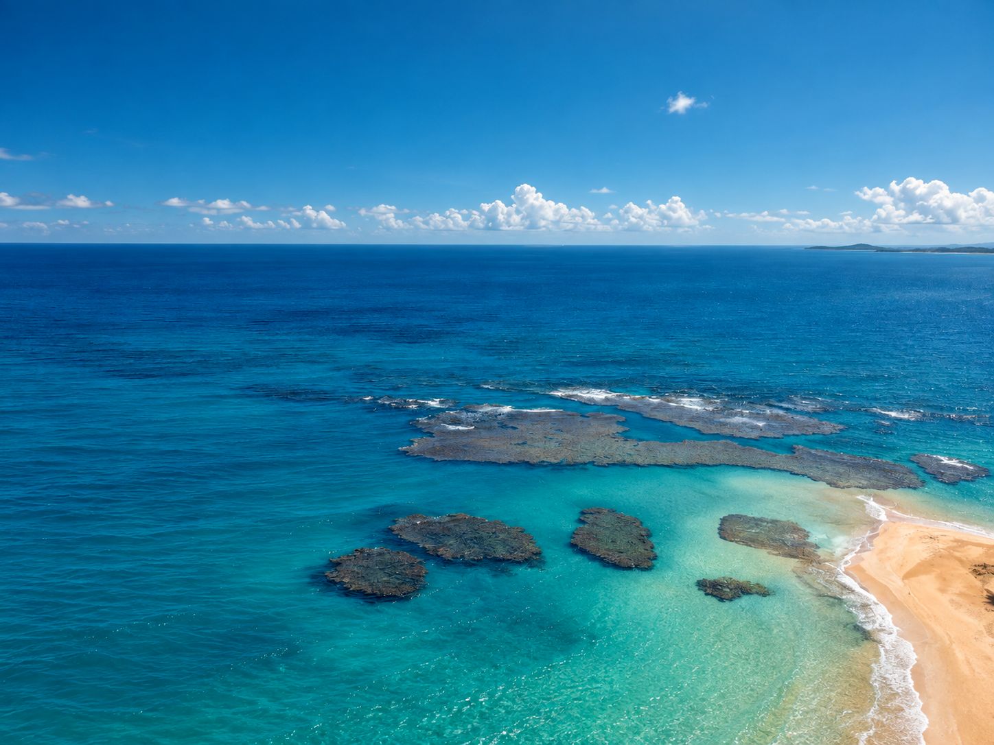 A coastal landscape with clear blue waters, rocky formations, and a sandy beach.