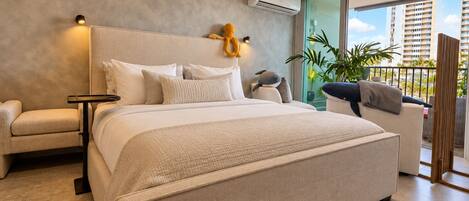 A modern bedroom with a large bed, a nightstand, a chair, and a balcony with a view of the city.