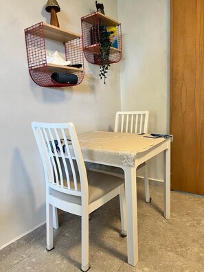 A dining area with a table and two chairs, a wall-mounted shelf with a plant, and a door to the right. - Serene Coastal Studio with King Bed & Balcony (Luquillo)