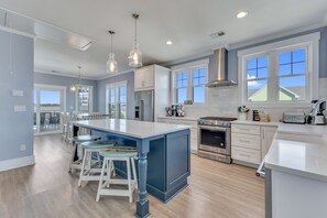 Une cuisine moderne dotée d’un grand îlot central, d’appareils électroménagers en acier inoxydable et de luminaires suspendus.