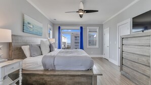 Un dormitorio con cama, mesita de noche, ventilador de techo y vistas al exterior.