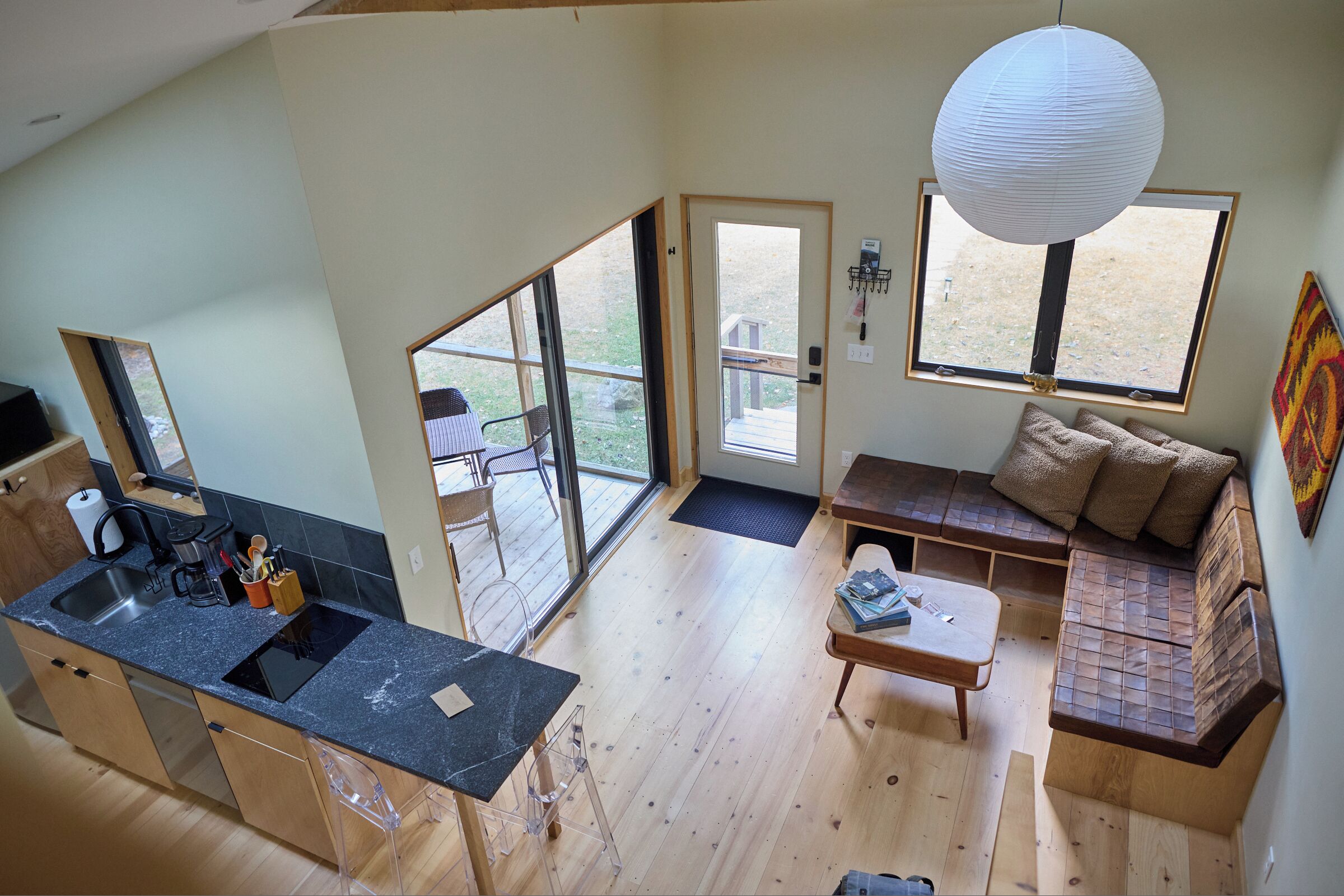 A spacious living area with a large window, a wooden sofa, a coffee table, and a kitchen area with a sink and countertop.
