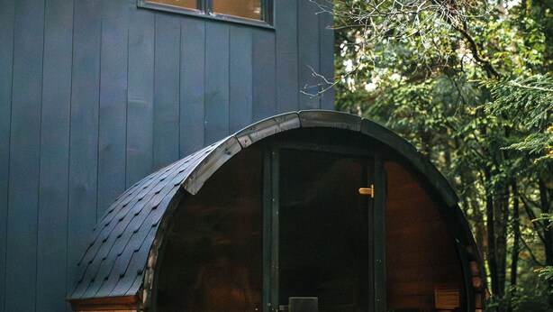 A cabin with a large wooden barrel-shaped structure attached to the main building, featuring a warm interior light.