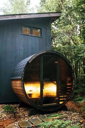 A cabin with a large wooden barrel-shaped structure attached to the main building, featuring a warm interior light. - Pond Cabin: Private Sauna+Near Beach+FirePit+Pond (Georgetown)
