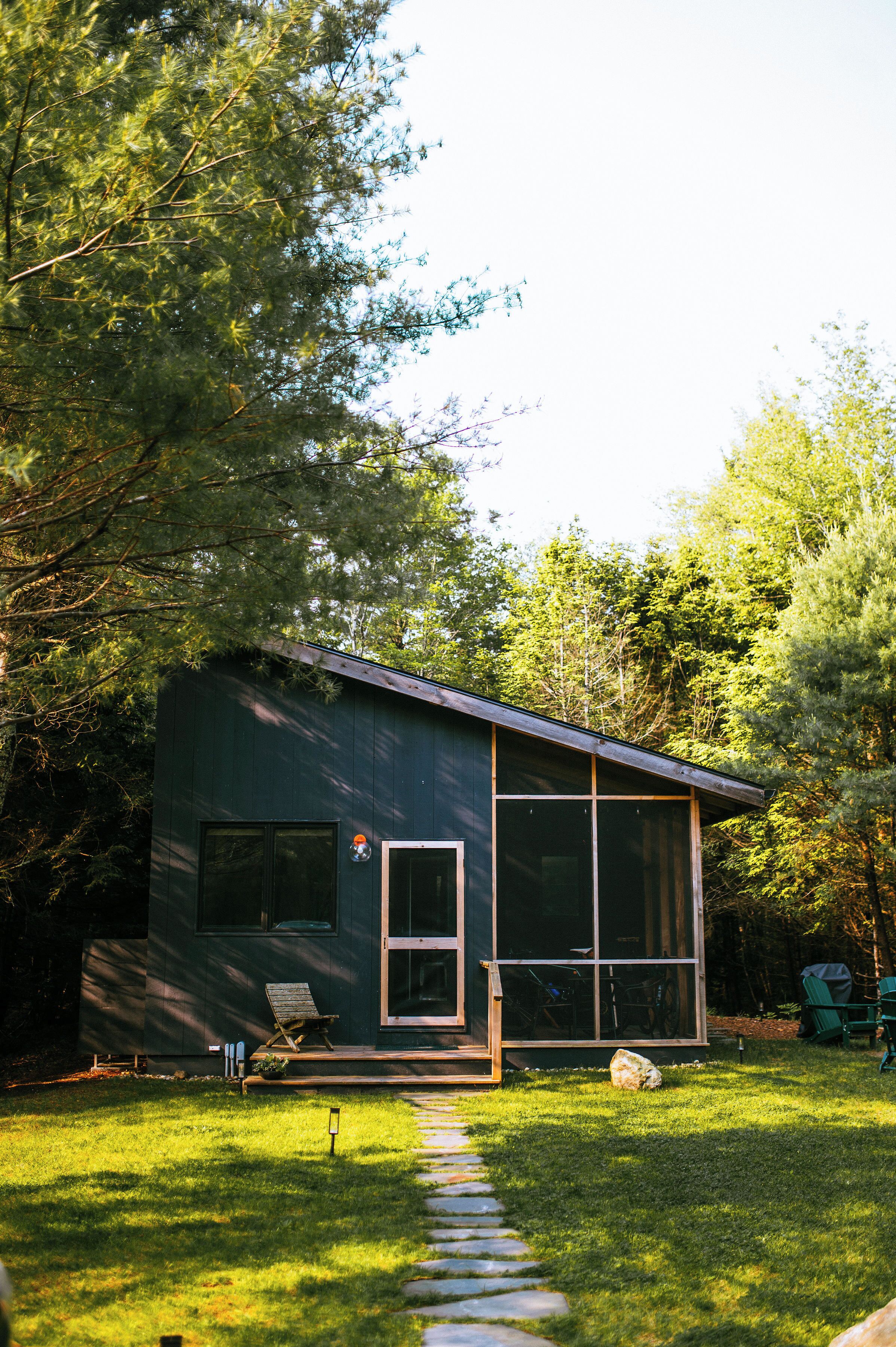 Een modern huis met een grote glazen deur, een klein portaal en een stenen pad dat naar de ingang leidt.