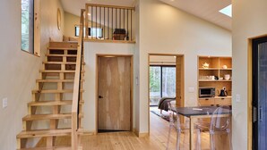A wooden staircase leading to a loft bedroom, a dining area with transparent chairs, and a kitchen with wooden shelves.