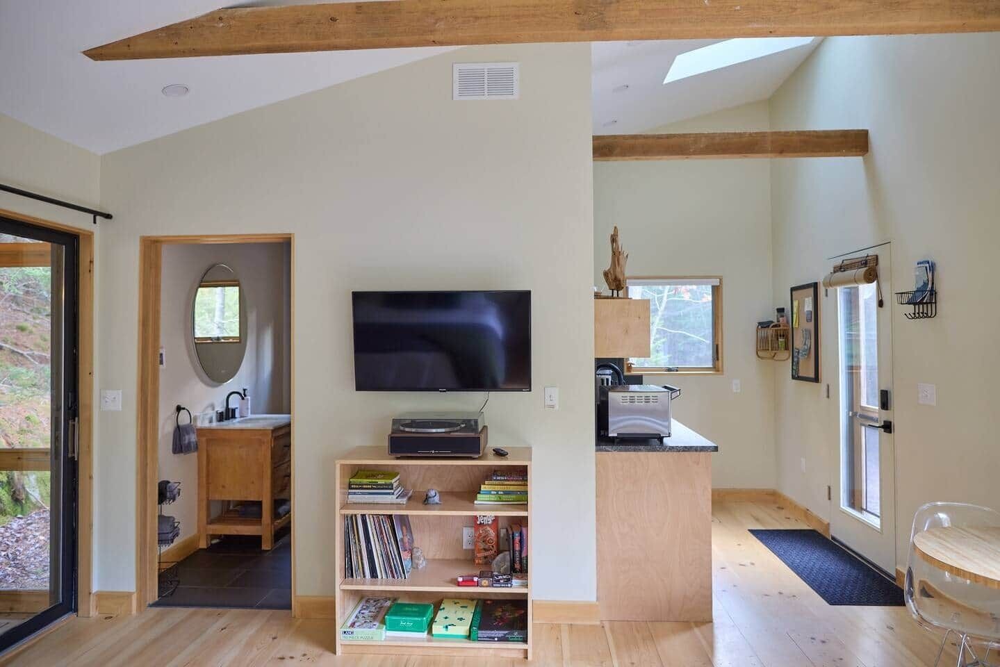 Un interior moderno con televisor, estanterías de madera, una zona de cocina y un ventanal grande.