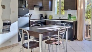 Une cuisine moderne avec des meubles de rangement en bois foncé, un réfrigérateur en acier inoxydable, une table à manger avec quatre chaises et une fenêtre donnant sur un paysage verdoyant.