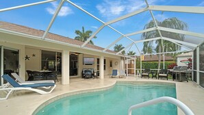An indoor pool area with a covered patio, lounge chairs, and a grill. - Bonitaville | Coastal Family Oasis w/ Heated Pool & Outdoor Living (Bonita Springs)