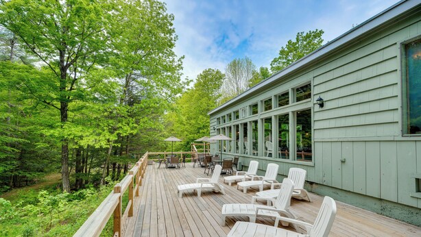 A wooden deck with lounge chairs and tables, surrounded by lush greenery and a building with large windows. - 3 Mi to Story Land: All-Season Family Condo (Bartlett)
